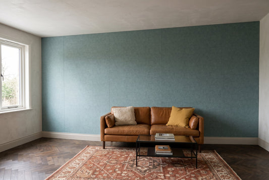 A living room wall clad in Pewter Grey felt acoustic wall panels behind a cognac leather sofa and a patterned rug