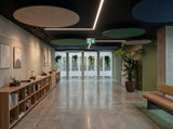 Round felt ceiling rafts in natural, green and navy hanging below a dark ceiling in a long office corridor