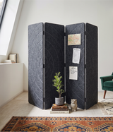 A four-panel folding room divider made of dark charcoal grey acoustic PET felt, styled in a bright room with a small potted plant, books, an owl figurine, a map, and sticky notes on its front panels.