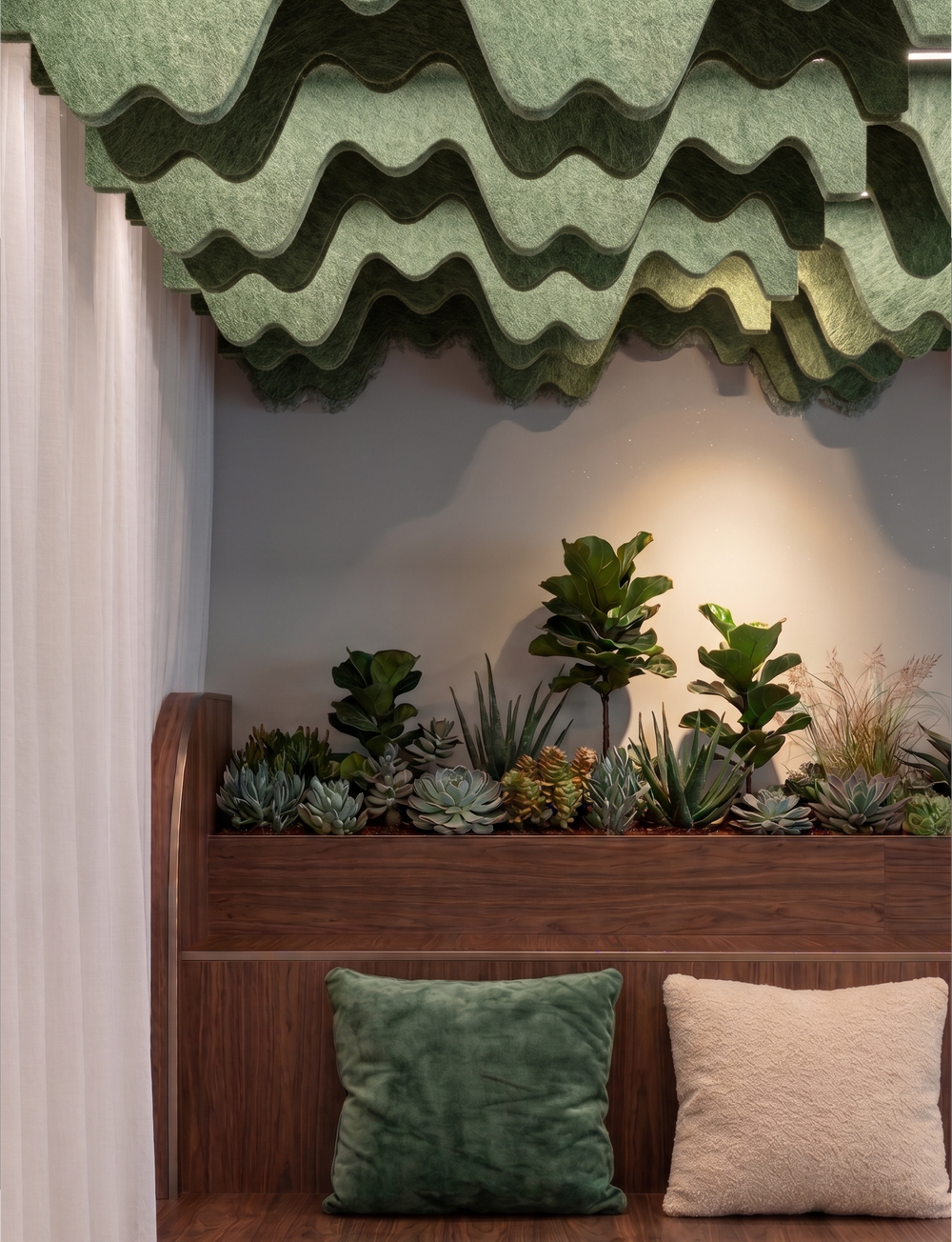 A styled interior corner featuring a wooden bench with two textured throw pillows, a built-in planter with green plants, and a compound wave PET felt acoustic raft above.