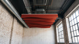 Drape felt ceiling baffles in Dark Rouge under an exposed industrial ceiling