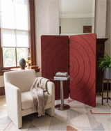 A red fabric folding screen with concentric circle patterns stands in a styled room next to a cream armchair and a small side table.