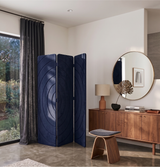 A navy blue three-panel folding screen with concentric circular patterns, styled in a modern room next to a window with dark curtains.