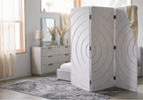 A three-panel folding room divider with a textured light gray fabric and concentric circle pattern, styled in a bright, modern bedroom next to a bed and dresser.