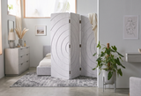 A three-panel folding room divider with a textured, circular wood-grain pattern in a light gray color, styled in a modern bedroom setting.