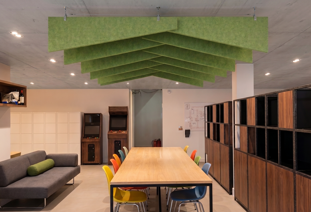 Apple green Felted trapezoid acoustic raft suspended above a meeting table in a bright office with timber storage